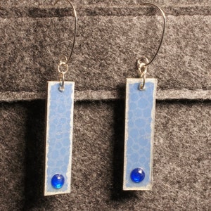May include: A pair of silver earrings with blue rectangular pendants and blue glass accents.