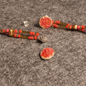 Peut inclure: Deux paires de boucles d'oreilles avec des perles rouges et dorées et un pendentif circulaire rouge et doré. Les boucles d'oreilles sont sur une surface grise.