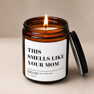 Peut inclure: Une bougie allumée dans un pot en verre ambré avec un couvercle noir. L'étiquette blanche porte le texte noir THIS SMELLS LIKE YOUR MOM, NATURAL COCONUT WAX, COTTON WICK, MADE IN CANADA, 10 oz et Candle Luxe. La flamme est jaune vif.