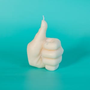 May include: A white candle shaped like a thumbs up gesture. The candle is on a turquoise background.