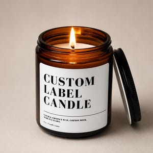 May include: A lit candle in an amber glass jar with a black metal lid. The white label features the black text CUSTOM LABEL CANDLE, followed by NATURAL COCONUT WAX, COTTON WICK, MADE IN CANADA, and 8 oz. / Candle Lume. The flame is bright yellow.