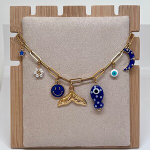 May include: A gold chain charm bracelet with blue and white enamel charms, including a crescent moon, a fish, a smiley face, a flower, and an evil eye.