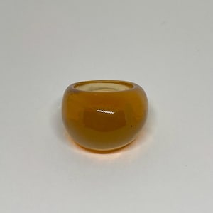 Peut inclure: Une large bague en verre de couleur ambre. La bague est lisse et arrondie, avec une finition brillante.