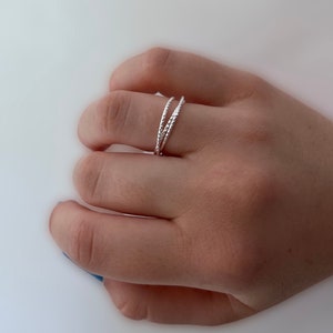 Op de afbeelding: Een zilveren ring met een textuurontwerp. De ring wordt aan een vinger gedragen.