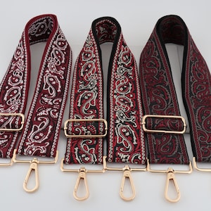 Puede incluir: Tres correas ajustables con estampado paisley y herrajes metálicos dorados. Las correas son rojas, negras y una combinación de rojo y negro.