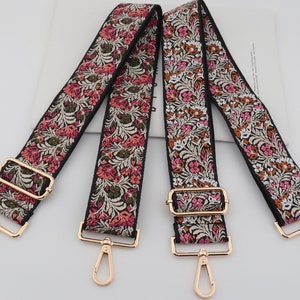 Puede incluir: Tres correas de tela con estampado floral y herrajes metálicos dorados, incluyendo una hebilla y un gancho. Las correas son negras con diseños florales rosas y blancos.
