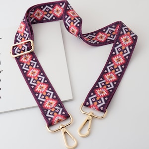 Może przedstawiać: Regulowany pasek z pozłacanymi metalowymi okuciami, w kolorze bordowym i białym z geometrycznym wzorem. Pasek ma geometryczny wzór z małymi sercami.