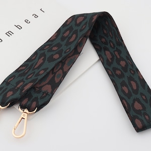 Puede incluir: Una correa ajustable con cierres de metal dorado, con estampado de leopardo verde y marrón. La correa está hecha de tejido tejido y tiene aproximadamente 3,8 cm de ancho.