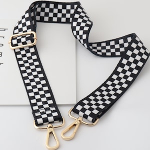 Könnte beinhalten: Schwarz-weiß kariertes Stoffband mit goldfarbener Metallbeschläge, einschließlich einer Schnalle und zwei Verschlüssen. Das Band ist etwa 3,8 cm breit.