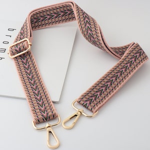 Puede incluir: Una correa ajustable con herrajes de metal dorado. La correa está hecha de tejido tejido y tiene un patrón de chevron rosa y verde.