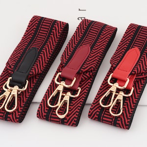 Może przedstawiać: Trzy czerwono-czarne paski z wzorami i złotymi metalowymi klamrami. Każdy pasek ma czerwoną skórzaną zakładkę na końcu.