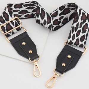 May include: An adjustable strap with a black and white leopard print design, featuring gold hardware and black leather accents. The strap has two gold swivel clips.