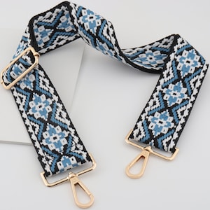 May include: A blue, white, and black patterned woven strap with gold metal clasps. The strap is approximately 1.5 inches wide.