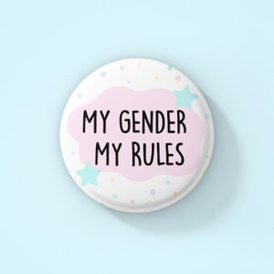 Może przedstawiać: Biały guzik z różową chmurką i napisem "MY GENDER MY RULES" w kolorze czarnym. Guzik jest ozdobiony pastelowymi niebieskimi gwiazdkami i kolorowymi kropkami.