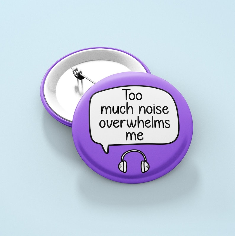 May include: Purple button badge with a white speech bubble that says "Too much noise overwhelms me".  A black and white drawing of headphones is below the speech bubble.