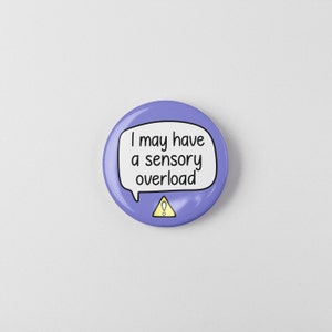 May include: Purple button with a white speech bubble that says "I may have a sensory overload" with a yellow exclamation point in a triangle.