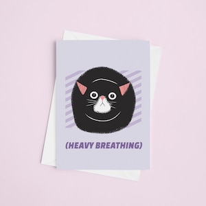 May include: A greeting card with a cartoon cat illustration. The cat is black with pink ears and a white muzzle, set against a light purple background with diagonal stripes. The text "(HEAVY BREATHING)" is below the cat. A white envelope is behind the card.