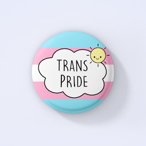May include: A round button with a pink, blue, and light blue transgender pride flag design. A white cloud with the text "TRANS PRIDE" is on top of the flag. A yellow sun with a smiling face is on the right side of the cloud.