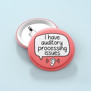 May include: A coral-coloured badge with the text "I have auditory processing issues" in a white speech bubble. The badge also features an ear graphic with sound waves. A second badge is visible in the background.
