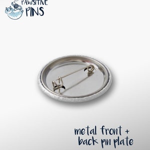 May include: The back of a round metal pin with a silver finish. The pin has a metal clasp on the back.