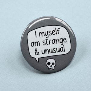 May include: A grey button with the text "I myself am strange & unusual" in a white speech bubble. A small white skull is below the text. The button is round and has a glossy finish.