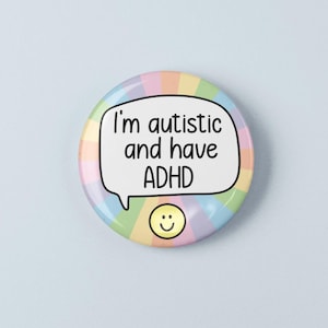 May include: A circular pin-back button featuring a pastel rainbow sunburst background. In the centre, a white speech bubble contains the black text 'I'm autistic and have ADHD'. Below the speech bubble is a small, yellow, smiling face icon.