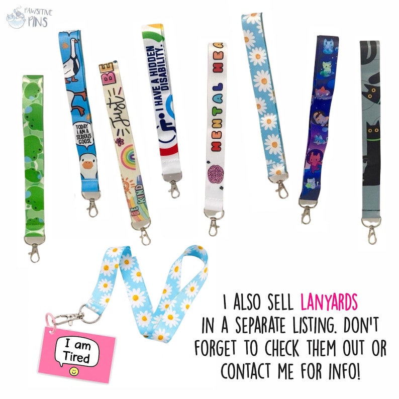 Op de afbeelding: Een verzameling kleurrijke lanyards met verschillende ontwerpen, waaronder madeliefjes, katten en inspirerende zinnen als "Just Be Kind" en "I Have a Hidden Disability". Elke lanyard heeft een metalen sluiting. Een roze label leest "I am Tired".
