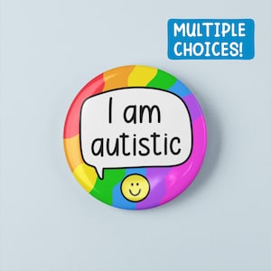 Puede incluir: Una chapa redonda con un fondo ondulado de colores del arcoíris. En el centro, un bocadillo blanco contiene el texto negro 'I am autistic'. Debajo del bocadillo, un pequeño icono de cara sonriente amarilla está impreso en la chapa.