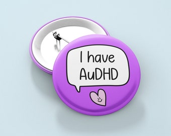 May include: Purple button with a white speech bubble that says "I have AuDHD" and a pink heart with a smiley face.