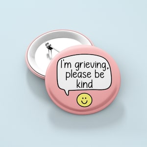 May include: Pink button with a white speech bubble that says "I'm grieving, please be kind" and a yellow smiley face.