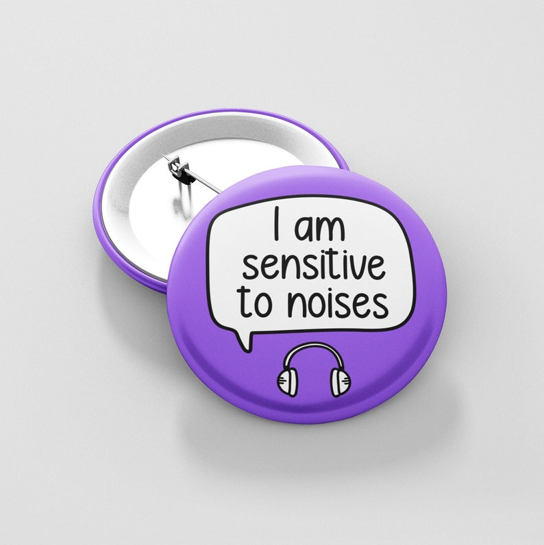 May include: Purple button with a white speech bubble that says "I am sensitive to noises" and a black and white drawing of headphones.