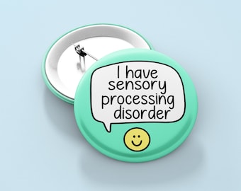 May include: A teal blue button with a white speech bubble that says "I have sensory processing disorder" and a yellow smiley face.