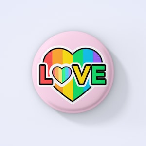 May include: A pink button featuring a rainbow heart with the word "LOVE" in black outlined letters. The heart is filled with rainbow stripes and has a smaller rainbow heart in the centre.