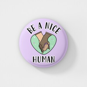 May include: Purple button with the text "Be a Nice Human" in black. A green heart with two hands holding each other is in the centre of the button.