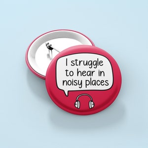 May include: Red button with a white speech bubble that says "I struggle to hear in noisy places".  The speech bubble has a black outline and a black headphone icon inside.