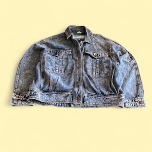 May include: A vintage acid wash denim jacket with two chest pockets and two side pockets. The jacket has a button-up front, button cuffs, and a classic collar. The denim is a faded blue with a mottled pattern.