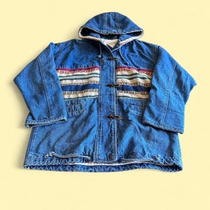 May include: A blue denim hooded jacket featuring a horizontal woven panel across the chest with stripes in red, white, blue, and green. The jacket includes a front closure with three metal toggle clasps and a drawstring cord at the bottom hem.