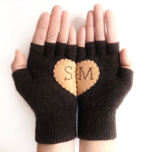 Könnte beinhalten: Braune fingerlose Handschuhe mit einem braunen Herzen, das auf der Rückseite aufgenäht ist. Das Herz hat die Buchstaben "S" und "M" aufgestickt.