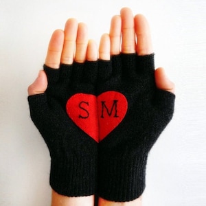 Könnte beinhalten: Schwarze fingerlose Handschuhe mit einem roten Herzen auf der Rückseite. Das Herz enthält die Buchstaben "S" und "M".