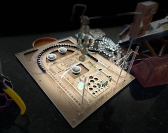 May include: A wooden Pendlebury Loom Board with a curved ruler, multiple holes, and a series of pegs. The board has a series of beads and other crafting supplies. The board is used for weaving and jewelry making.