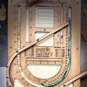 May include: A wooden design board with scales in inches and centimetres. It features curved and straight tracks, with beads and a wire gauge. The board has the text "Pendlebury" and "Parrett Mountain" on it. The board is made in Sherwood.