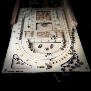 May include: A wooden jewelry making tool with a circular guide for measuring necklace lengths in inches. The tool has a label that reads "pendle & bury" and "Made in Sherwood, Oregon, USA".