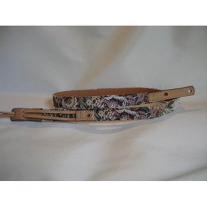 May include: Two brown leather guitar straps with a floral pattern. The straps are woven with a multi-coloured floral design.