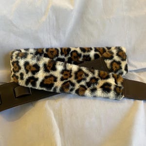 Puede incluir: Una correa de guitarra de cuero marrón con acolchado de piel de leopardo blanco y marrón.