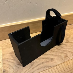 Puede incluir: Un organizador de plástico negro con una correa para llevar. El organizador tiene una ranura para guardar objetos.