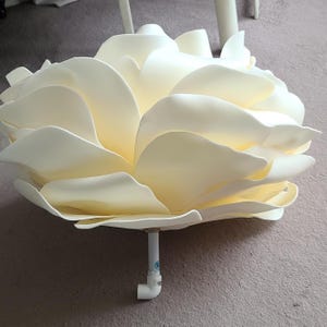 May include: A large, white foam flower with multiple layers of petals. The flower is attached to a white PVC pipe.