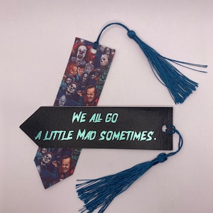 May include: Two horror-themed bookmarks with teal tassels. One bookmark features a collage of horror movie characters. The other is black with the text "WE ALL GO A LITTLE MAD SOMETIMES" in teal.