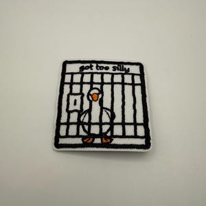 Op de afbeelding: Geborduurde patch met een cartoon gans in een kooi. De gans is wit met een oranje snavel en poten. De kooi is zwart en wit, met de woorden "got too silly" in oranje erboven.