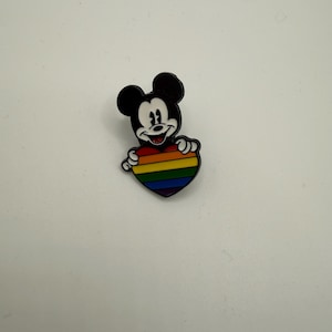 May include: A Mickey Mouse pin in black and white, holding a rainbow heart. The pin shows Mickey Mouse with a black body and ears. The heart is a vibrant rainbow of colours.