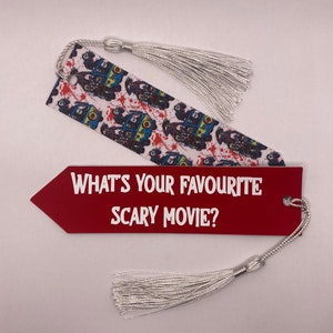 May include: Two bookmarks with silver tassels. One is red with the text "WHAT'S YOUR FAVOURITE SCARY MOVIE?" in white. The other is white with a pattern of zombie-themed vans and red splatters.
